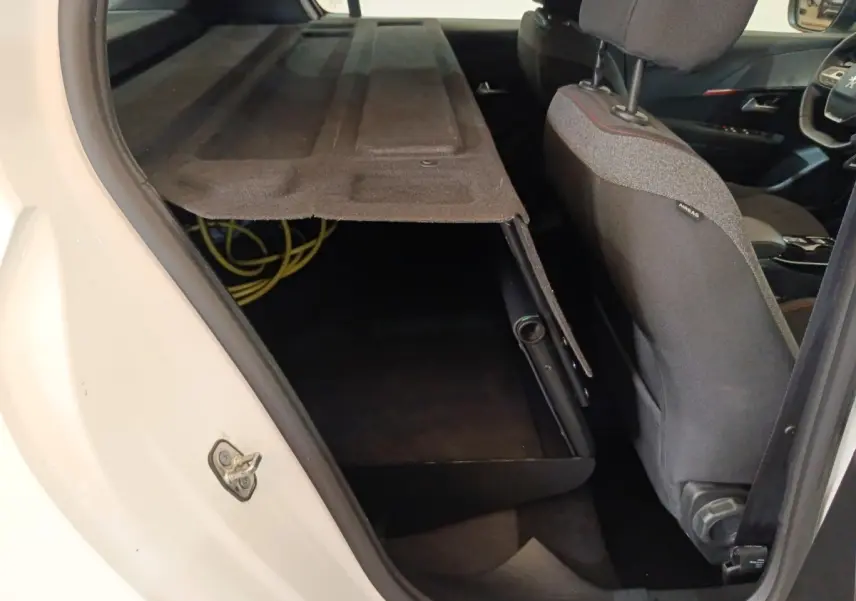 Vue intérieure côté arrière droit d'une Peugeot 208 électrique blanche avec banquette rabattue et coffre ouvert.