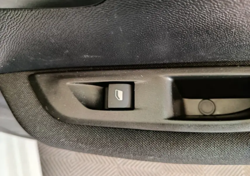 Bouton de commande de lève-vitre sur la porte intérieure noire d'une Peugeot 208 électrique blanche, vue rapprochée.