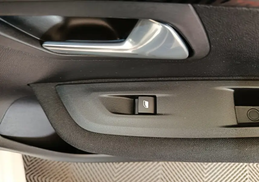 Détail de la poignée intérieure et bouton de lève-vitre côté conducteur d'une Peugeot 208 électrique blanche, vue rapprochée.