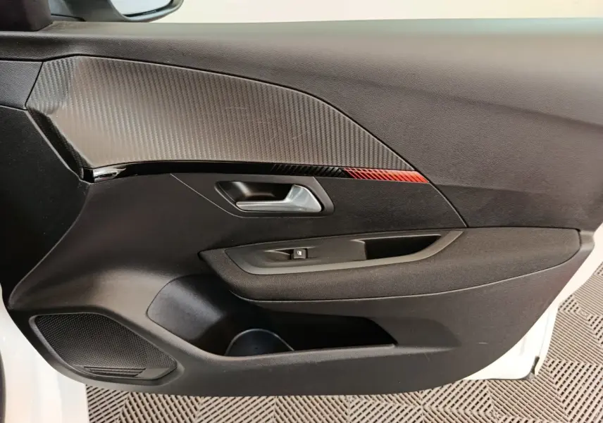 Vue intérieure côté gauche de la porte avant d’une Peugeot 208 électrique blanche avec insert décoratif noir et rouge.