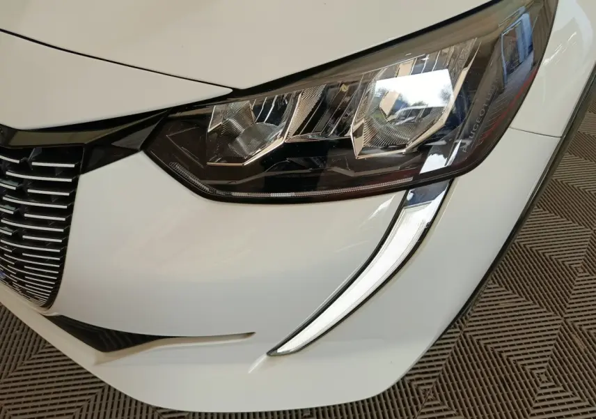 Gros plan sur le phare avant droit blanc de la Peugeot 208 électrique avec signature lumineuse LED distinctive.