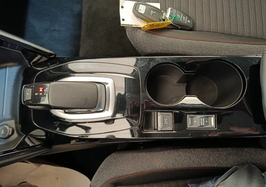 Vue plongeante sur la console centrale noire de la Peugeot 208 électrique avec levier de vitesses et clés posées sur siège gris.
