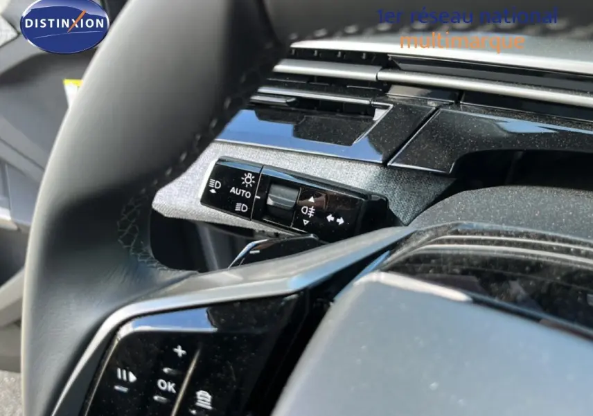 Gros plan sur le volant noir et la commande des phares du Peugeot 5008 gris Artense, intérieur moderne et épuré.