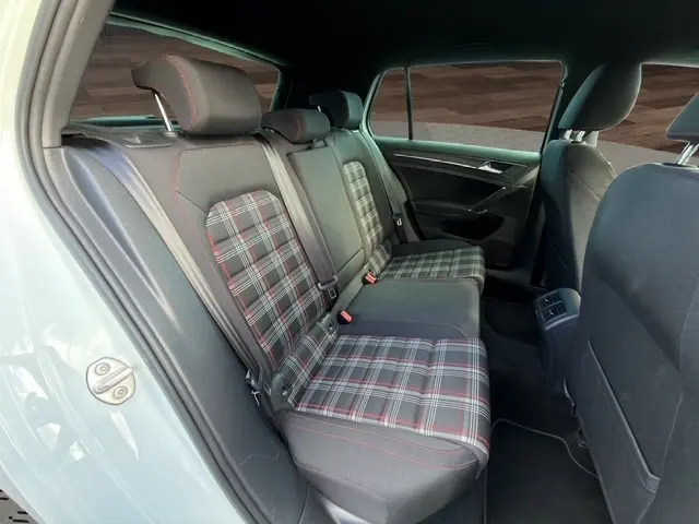 Vue intérieure arrière gauche de la Volkswagen Golf GTI Performance blanche, sièges arrière à motif tartan avec surpiqûres rouges.