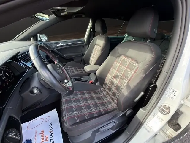 Vue intérieure côté conducteur de la Volkswagen Golf GTI Performance blanche, sièges à motif tartan et volant cuir alu multifonctions.