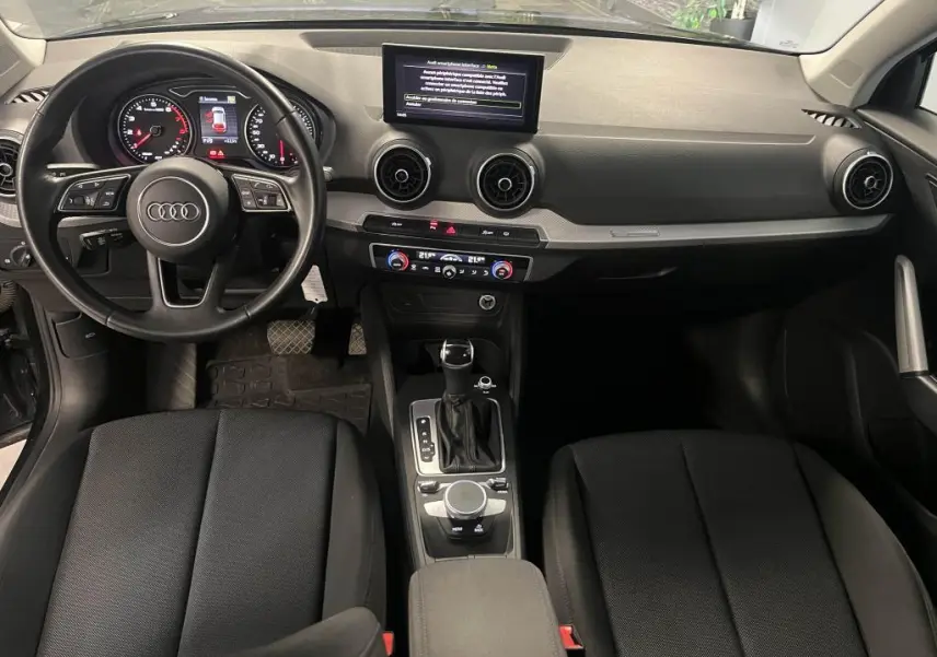 Intérieur Audi Q2 2022 vu de face, tableau de bord noir avec écran central et volant multifonction cuir.