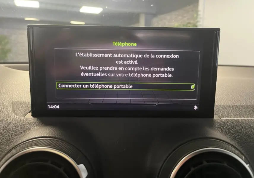 Écran central de l'Audi Q2 2022 affichant la connexion Bluetooth pour téléphone portable, entouré de grilles d'aération rondes noires.
