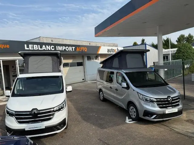 Vue avant de deux Renault Trafic Fourgon blanc glacier avec toit relevé, stationnés devant un garage automobile.