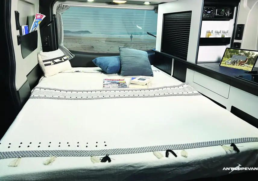 Vue intérieure arrière du van aménagé Renault Trafic blanc glacier, montrant le lit avec coussins et rangements intégrés.