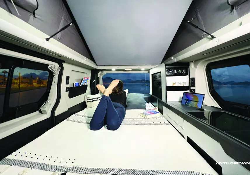 Intérieur du Renault Trafic Van Aménagé blanc, vue arrière sur le lit avec toit relevable et rangements intégrés.