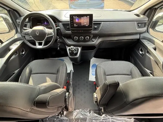 Vue intérieure avant du Renault Trafic Fourgon blanc glacier, tableau de bord avec écran tactile et sièges pivotants noirs.