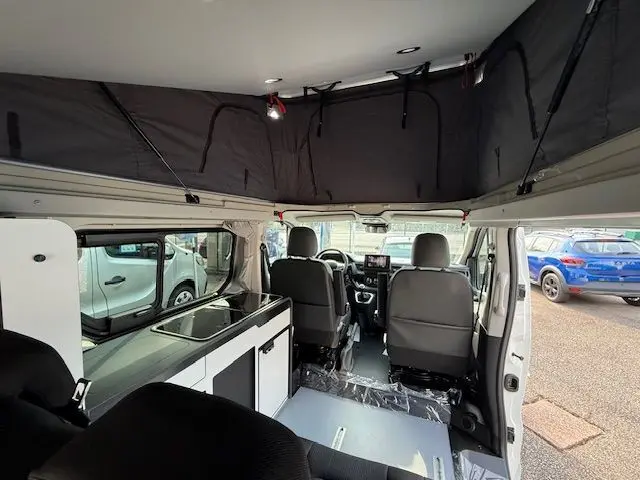 Intérieur du Renault Trafic Fourgon blanc glacier vu de l'arrière, montrant l'aménagement van avec toit relevable noir et cuisine intégrée.