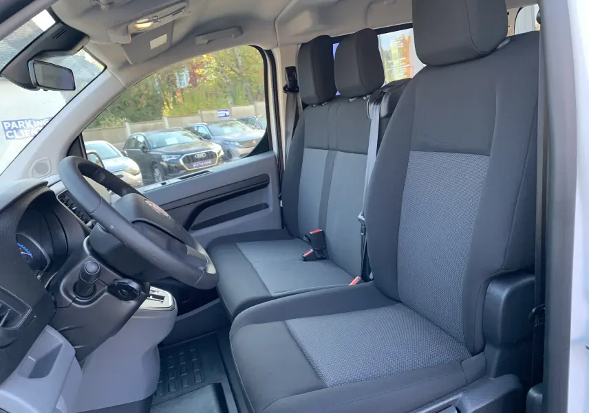 Vue intérieure côté conducteur du Fiat Scudo Combi 2022 blanc, montrant les sièges tissu gris et le volant noir.