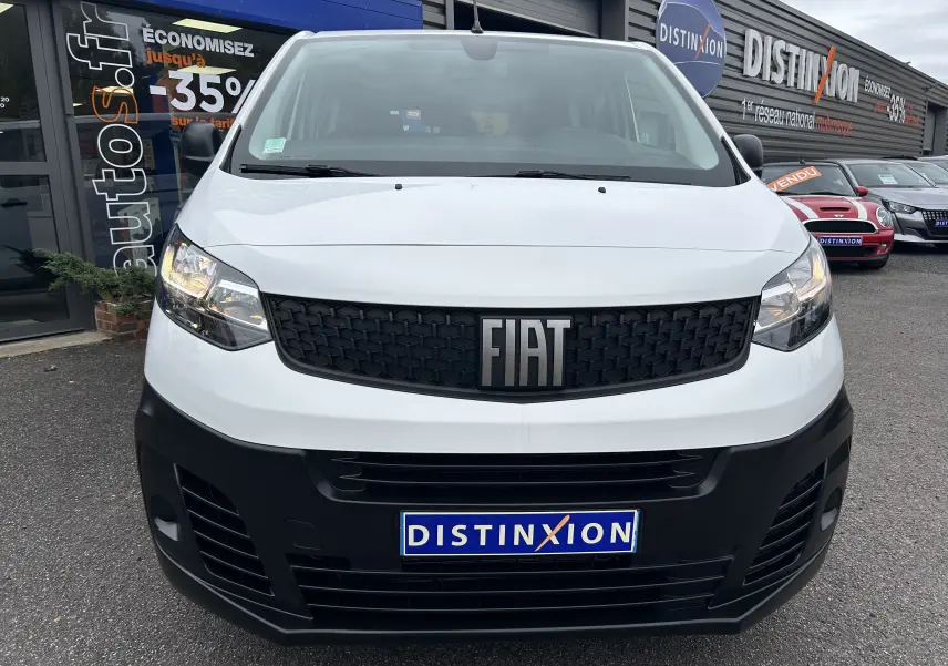 Vue frontale d'un FIAT Scudo Combi blanc avec calandre noire et logo FIAT bien visible, stationné devant un concessionnaire.
