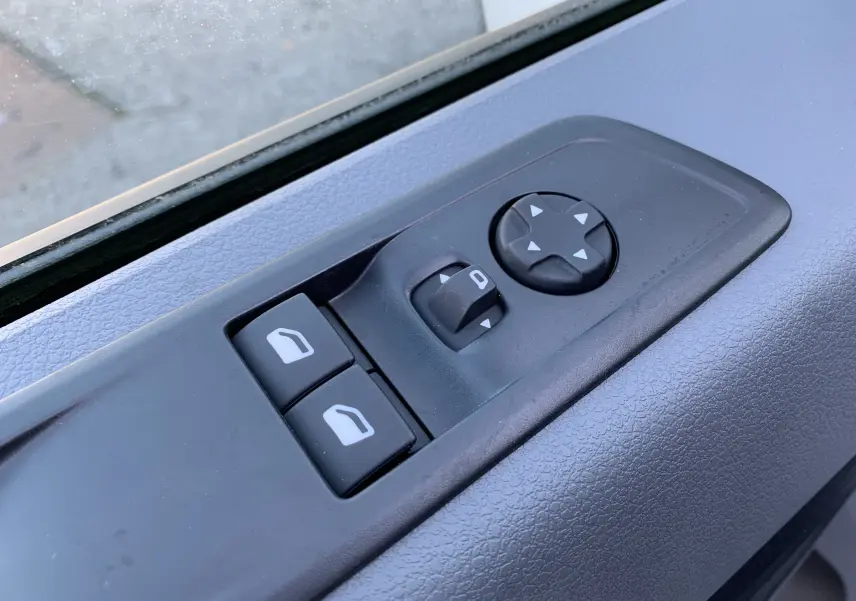Gros plan sur les commandes de lève-vitres et réglage des rétroviseurs côté gauche du Fiat Scudo Combi blanc électrique 2022.