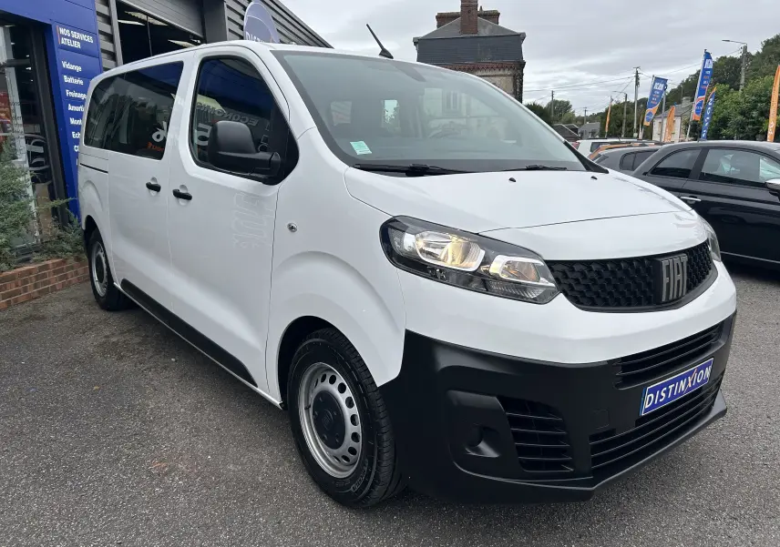 Fiat Scudo Combi électrique blanc vu en 3/4 avant droit, avec calandre noire et phares allumés.