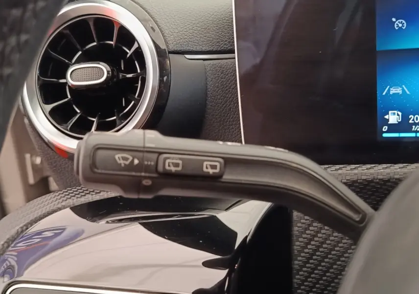 Détail intérieur du levier d’essuie-glace avec aérateur rond et écran tactile du tableau de bord d’une Mercedes Classe A gris clair.