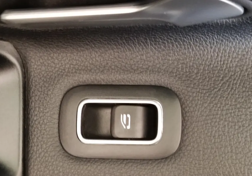 Gros plan sur le bouton d'ouverture du coffre intégré dans le revêtement noir texturé intérieur d'une Mercedes Classe A gris clair.