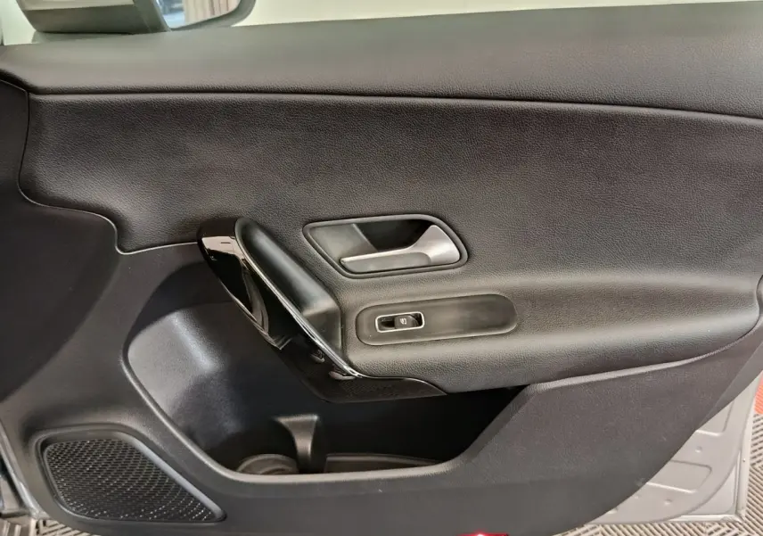 Vue intérieure du panneau de porte côté gauche noir de la Mercedes Classe A 180 Business Line 2020 avec poignée argentée et commande de fenêtre.