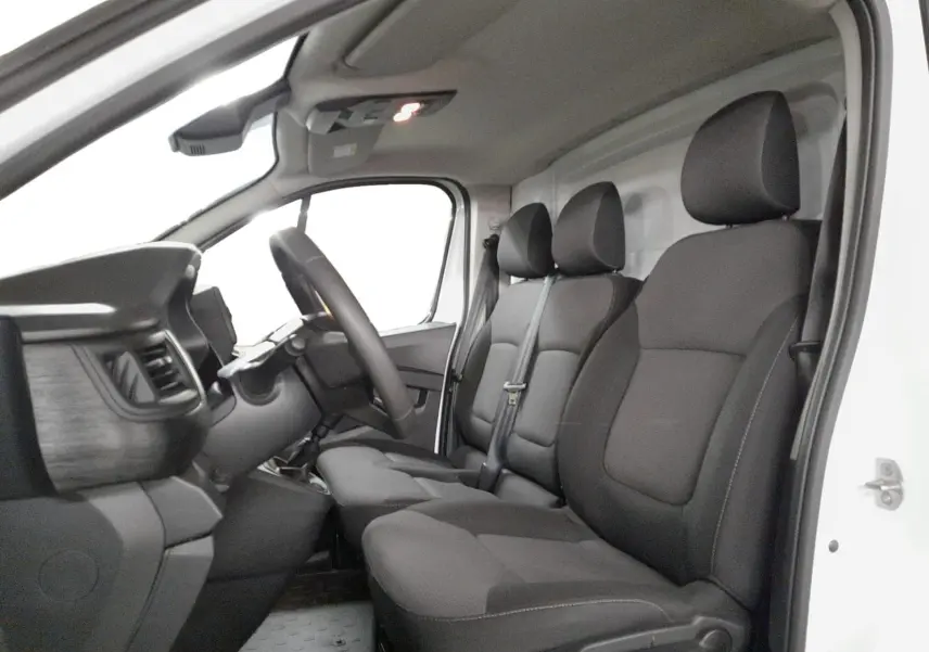 Vue intérieure côté conducteur du Renault Trafic Fourgon 2024 blanc, montrant les sièges tissu noirs et le tableau de bord.