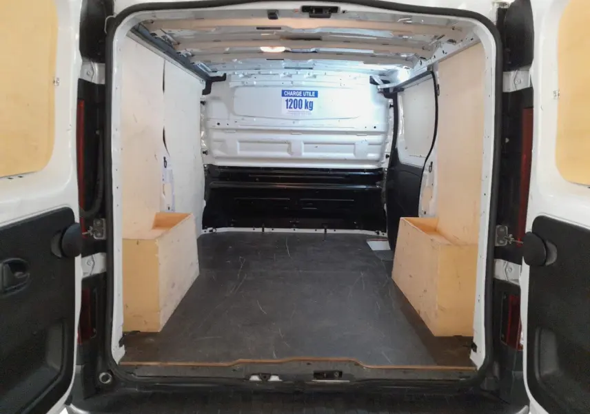 Vue arrière intérieure du Renault Trafic Fourgon blanc minéral 2024, montrant l’espace de chargement vide avec panneaux bois.