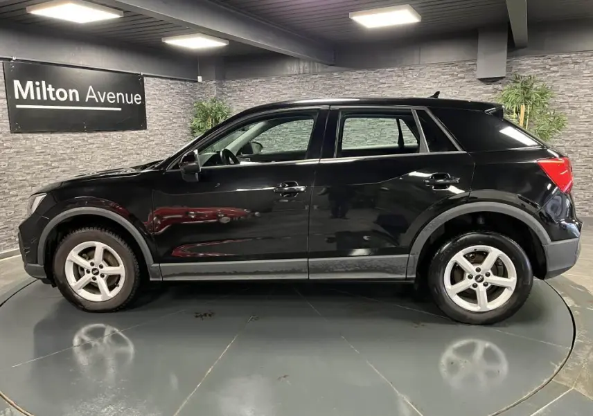 Profil côté gauche d'un Audi Q2 noir brillant 2022 avec jantes aluminium 16 pouces dans un showroom intérieur.