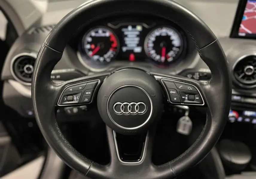 Vue intérieure centrée sur le volant cuir multifonction et la console avec écran de navigation de l'Audi Q2 noire.