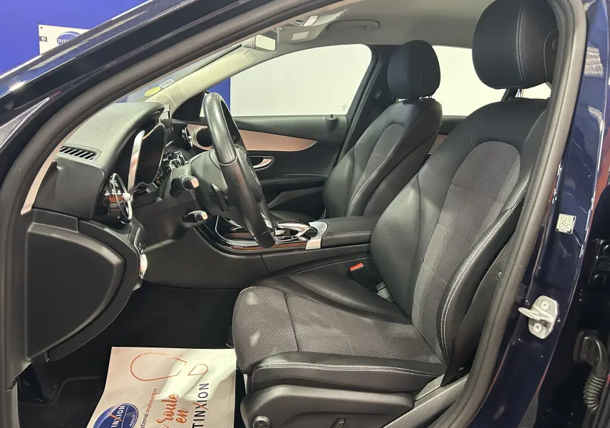 Vue intérieure côté conducteur d'une Mercedes Classe C 200d bleu, sièges en cuir noir et tableau de bord moderne.