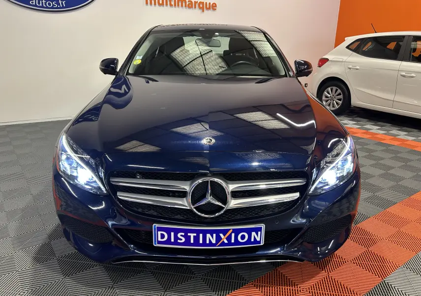 Vue frontale d'une Mercedes Classe C 200d bleu avec phares allumés et calandre chromée dans un showroom.