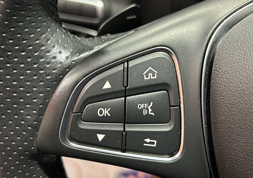 Gros plan sur les commandes multifonctions à gauche du volant en cuir perforé d'une Mercedes Classe C 200d 2018.