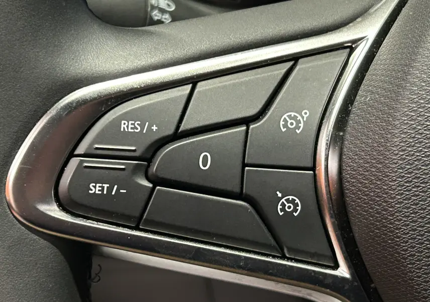Gros plan sur les commandes de régulateur de vitesse au volant d’une Renault Clio V gris Rafale Métal.