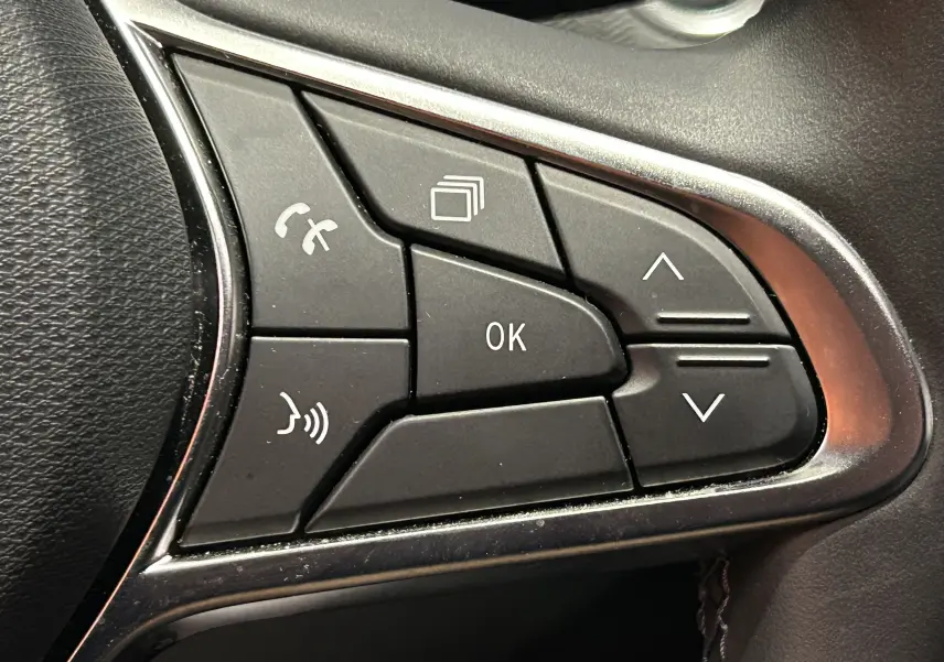 Gros plan sur les commandes multifonctions noires du volant de la Renault Clio V gris Rafale métal.