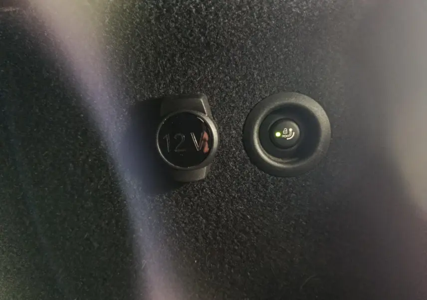 Détail intérieur montrant la prise 12V et le bouton de commande de ventilation additionnelle sur fond noir.