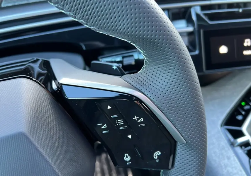 Gros plan sur la partie gauche du volant en cuir perforé gris avec commandes tactiles du Peugeot 3008 Hybrid 2025.