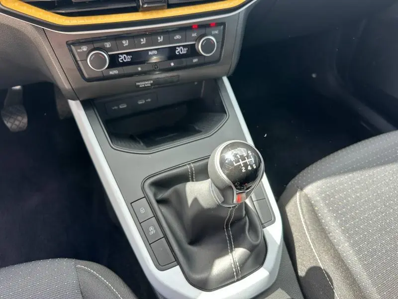 Vue rapprochée du levier de vitesse manuel et de la console centrale du SEAT Arona blanc, avec sièges tissu gris.
