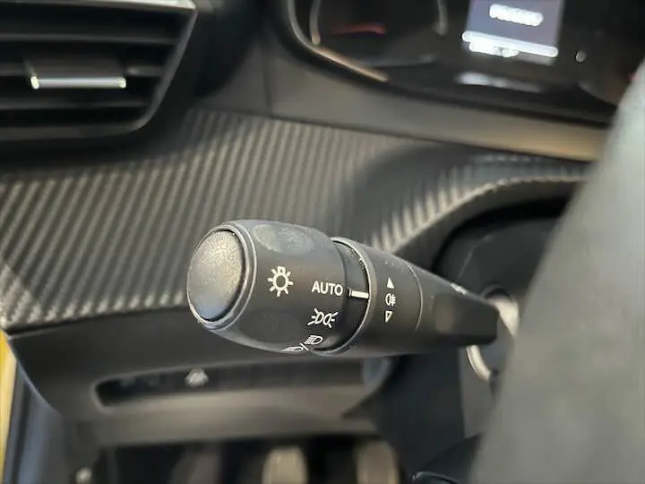 Gros plan sur la commande d'éclairage à gauche du volant dans l'habitacle d'une Peugeot 208 rouge Elixir Metal.