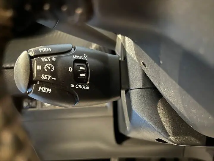 Gros plan sur la commande de régulateur de vitesse noire dans l'habitacle d'une Peugeot 208 rouge Elixir Metal.