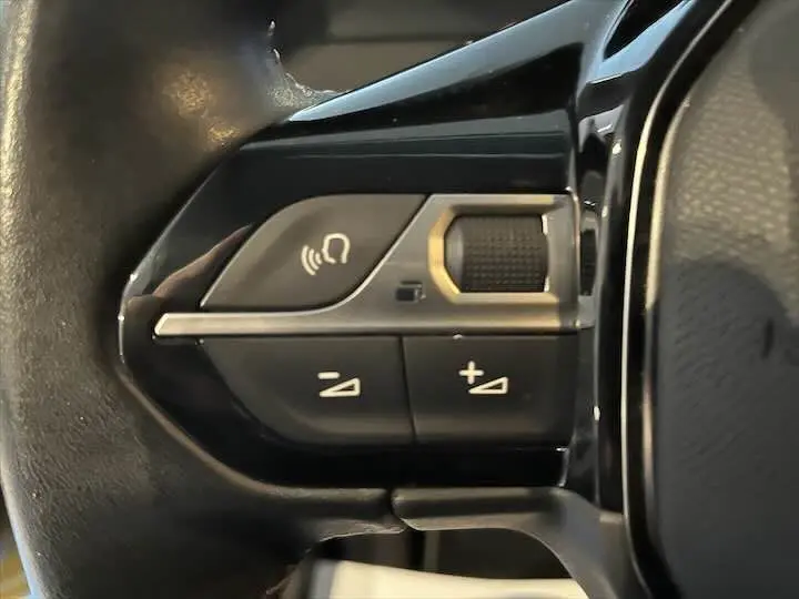 Gros plan sur les commandes de volume et téléphone intégrées au volant noir du Peugeot 208 Rouge Elixir Metal.