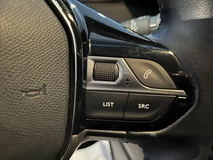 Gros plan sur les commandes du volant noir de la Peugeot 208 rouge Elixir, avec boutons LIST, SRC et appel téléphonique.