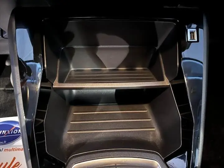 Gros plan sur le rangement central noir brillant de la Peugeot 208 rouge Elixir avec port USB visible à droite.