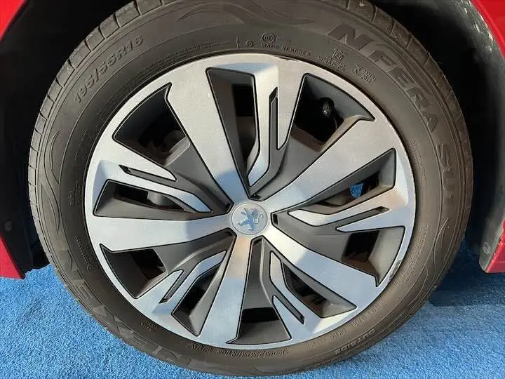 Gros plan sur la roue avant droite d'une Peugeot 208 rouge Elixir Metal avec jante alliage au design moderne.