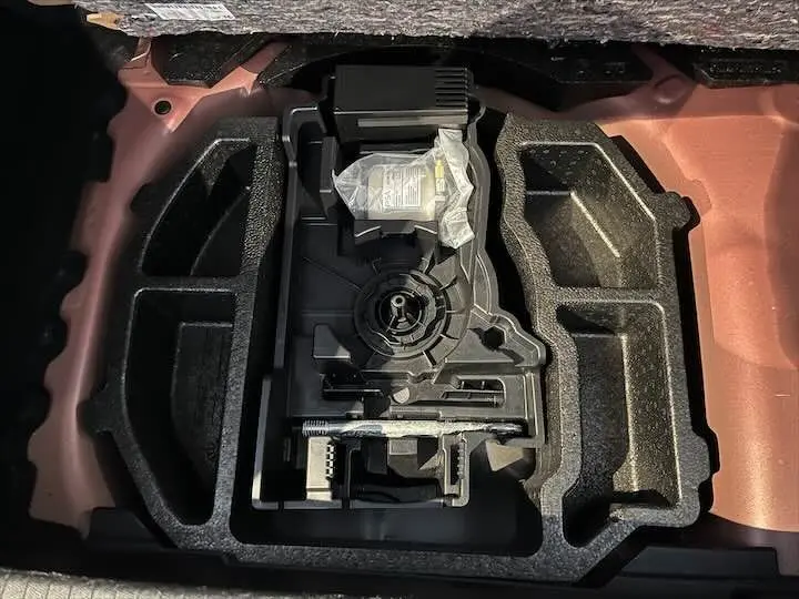 Compartiment de rangement sous le coffre d'une Peugeot 208 rouge Elixir Metal, montrant l'organisation des outils et accessoires.