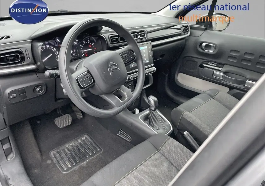Intérieur de la Citroën C3 2023 côté conducteur, tableau de bord moderne avec volant multifonction et sellerie tissu gris.