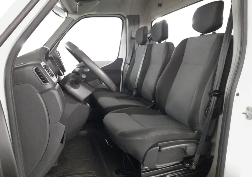 Vue intérieure côté conducteur du Renault Master blanc 2024, montrant les sièges noirs et le tableau de bord simple.