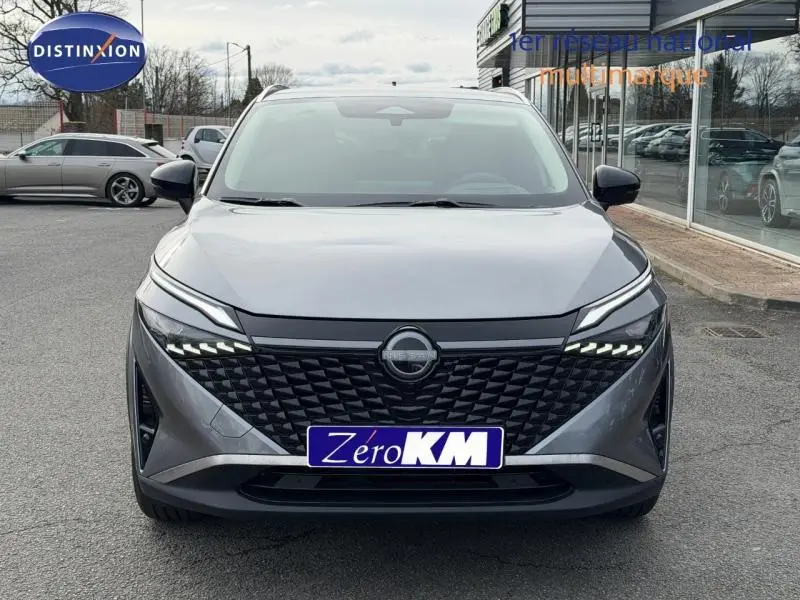 Vue avant d'un Nissan Qashqai Hybrid e-POWER 2025 gris squale métallisé avec calandre noire et feux LED distinctifs.