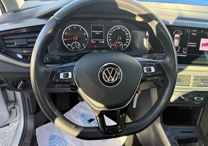Vue intérieure centrée sur le volant noir de la Volkswagen Polo 1.0 TSI 95 Lounge Business avec tableau de bord et écran multimédia.