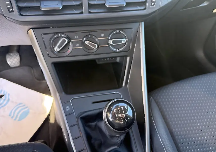 Vue intérieure centrée sur la console centrale d'une Volkswagen Polo gris métal 2021 avec levier de vitesses manuel et commandes climatiques.