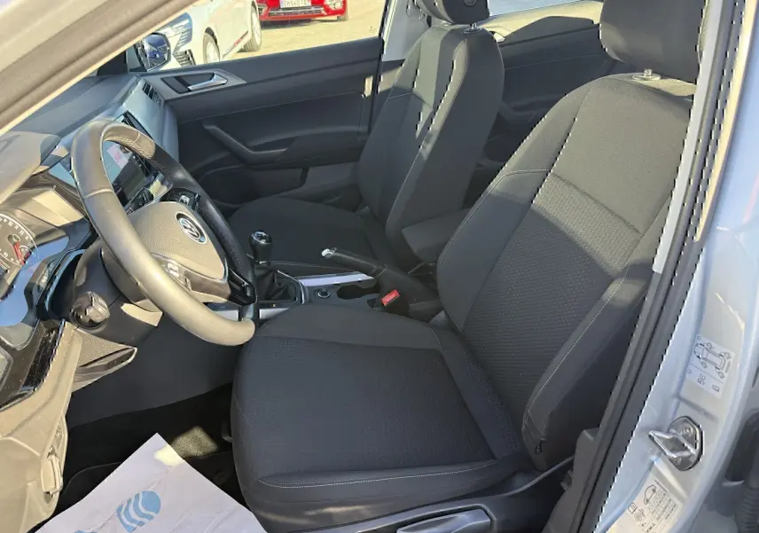 Vue intérieure côté conducteur de la Volkswagen Polo gris métal 2021, avec sièges noirs et boîte manuelle visible.