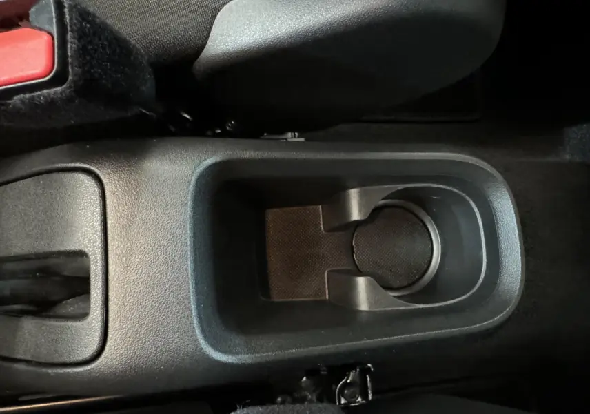 Gros plan sur le porte-gobelet central noir et la console entre les sièges avant d'une Citroën C3 gris foncé.