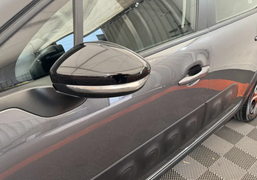 Gros plan sur le rétroviseur noir et la porte côté gauche d'une Citroën C3 gris foncé avec protection latérale noire.